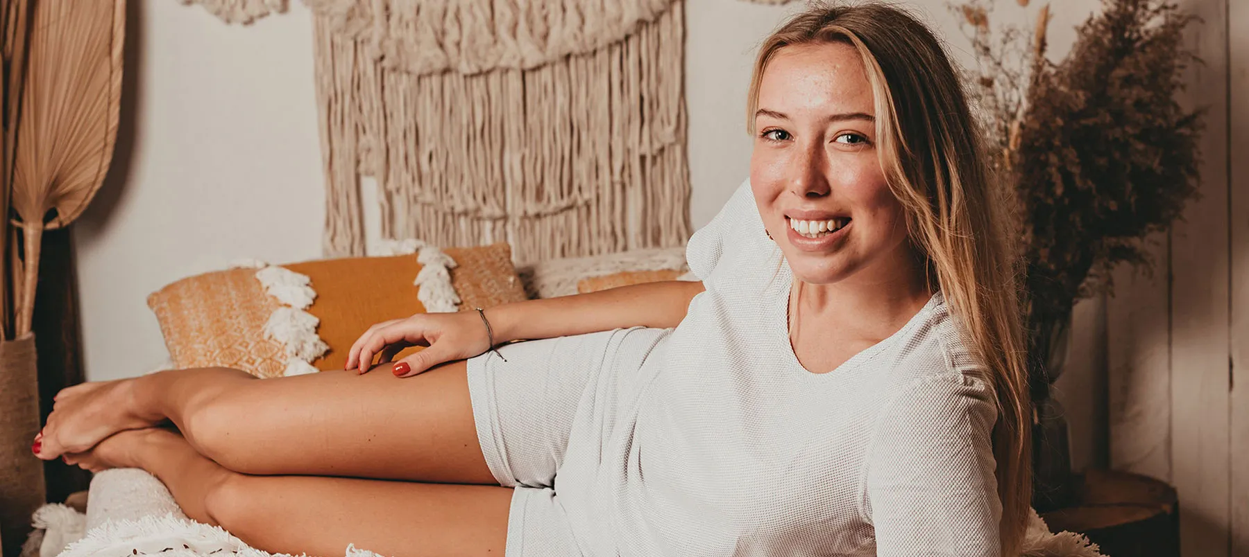 Junge Frau liegt entspannt auf einem Bett in gemütlichem Ambiente und trägt ein helles Abschirmshirt – stilvoller Schutz vor Elektrosmog für den Alltag.